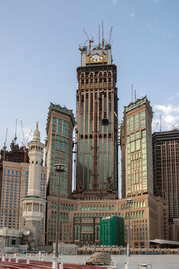 View of the Makkah Towers under construction with multiple cranes and scaffolding visible against a clear blue sky in Makkah Makkah Province Saudi Arabia. View of the Makkah Towers under construction with multiple cranes and scaffolding visible against a clear blue sky in Makkah Makkah Province Saudi Arabia.