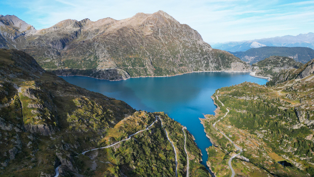 Aerial view of Barrage d Emosson with its turquoise reservoir surrounded by rugged alpine mountains and winding roads in Finhaut Valais Switzerland.