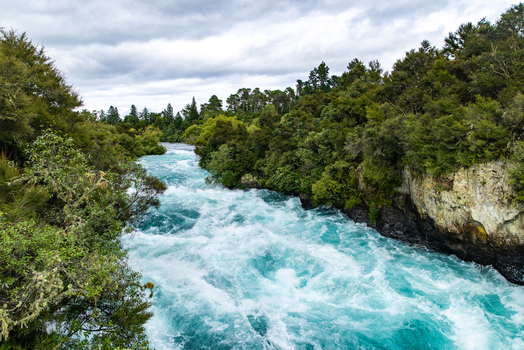 View of the turquoise Huka Falls churning powerfully between lush green banks under a cloudy sky Huka Falls Waikato Region New Zealand. View of the turquoise Huka Falls churning powerfully between lush green banks under a cloudy sky Huka Falls Waikato Region New Zealand.