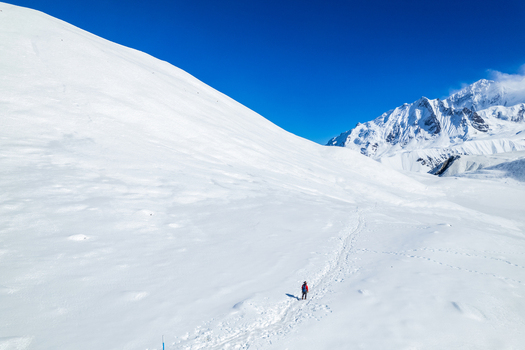 Aerial view of a lone hiker trekking through a vast pristine snow covered mountain landscape under a clear blue sky in the Himalayas Nepal.