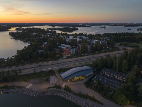 Aerial view of Koivusaari island featuring modern architecture coastal waters lush greenery and a highway at sunset in Helsinki Uusimaa Finland.