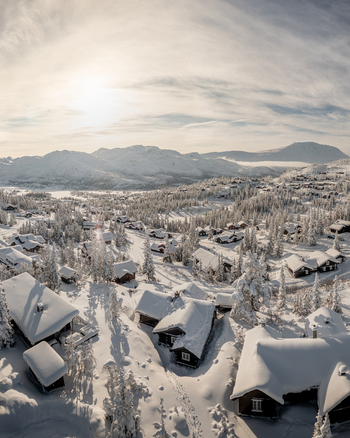 Aerial view of Gaustablikk Fjellresort featuring snow covered wooden cabins nestled among winter trees with majestic mountains in the background in Rjukan Telemark Norway. Aerial view of Gaustablikk Fjellresort featuring snow covered wooden cabins nestled among winter trees with majestic mountains in the background in Rjukan Telemark Norway.