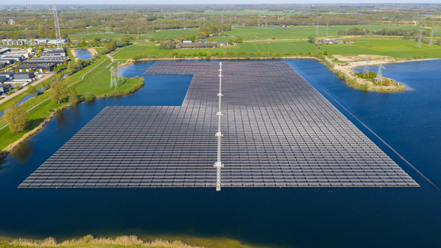 Aerial view of a large floating solar farm on a blue lake surrounded by green fields and industrial buildings in Zwolle Overijssel Netherlands. Aerial view of a large floating solar farm on a blue lake surrounded by green fields and industrial buildings in Zwolle Overijssel Netherlands.