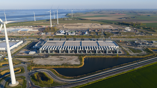 Aerial view of a large industrial data center facility and wind turbines along the coast under a clear sky in Eemshaven Groningen Netherlands. Aerial view of a large industrial data center facility and wind turbines along the coast under a clear sky in Eemshaven Groningen Netherlands.