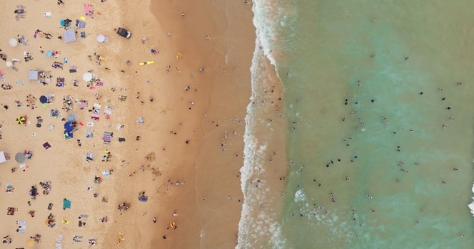 Aerial view of a crowded beach with people sunbathing on the sand and swimming in the turquoise ocean water in Sydney New South Wales Australia. Aerial view of a crowded beach with people sunbathing on the sand and swimming in the turquoise ocean water in Sydney New South Wales Australia.