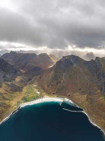 Aerial view of the dramatic coastal landscape of Senja with rugged mountains a sandy beach and a small harbor under a cloudy sky in Senja Troms Norway.