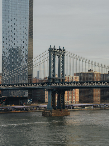 View of the Manhattan Bridge with its blue steel structure and suspension cables set against a backdrop of modern glass skyscrapers and residential buildings in New York New York United States.