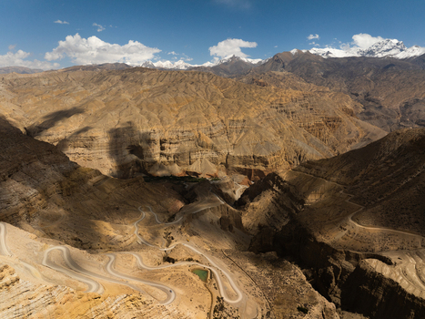 Aerial view of a winding mountain road snaking through a rugged arid canyon landscape with snow capped Himalayan peaks in the distance Nepal.