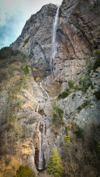 Aerial view of cascading water plunges down a rugged rocky mountain face a ribbon of white against the stark grey stone Sallanches Auvergne Rhône Alpes France. Aerial view of cascading water plunges down a rugged rocky mountain face a ribbon of white against the stark grey stone Sallanches Auvergne Rhône Alpes France.