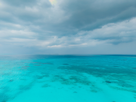 Aerial view of the turquoise sea meeting the horizon under a sky heavy with rain clouds Vashafaru Island Thiladhummathi Atoll Maldives. Aerial view of the turquoise sea meeting the horizon under a sky heavy with rain clouds Vashafaru Island Thiladhummathi Atoll Maldives.