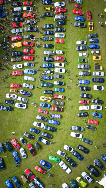 Aerial view of colorful sports cars and vintage vehicles parked in rows on a green field during a car show with people walking around La Chapelle de Guinchay Bourgogne Franche Comte France.
