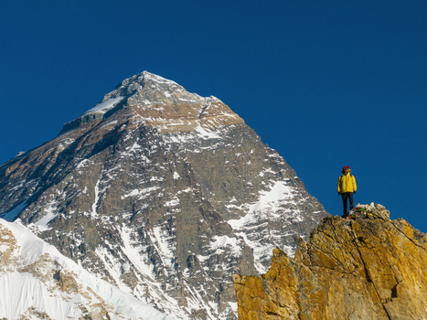 Aerial view of a climber in a yellow jacket standing on a rocky summit with the majestic Mount Everest in the background Nepal.