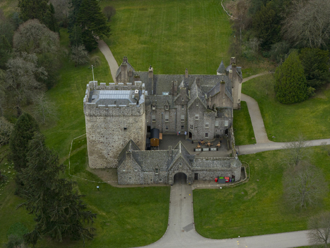 Aerial view of Drum Castle featuring its historic stone tower and courtyard surrounded by lush green lawns and woodland in Drumoak Scotland United Kingdom.