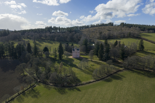 Aerial view of Craigievar Castle the iconic pink tower house nestled among lush green fields and dense woodland under a bright sky Craigievar Scotland United Kingdom.