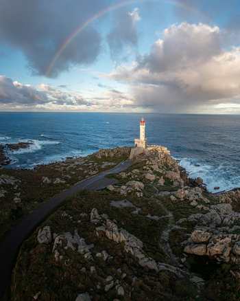Aerial view of Faro de Punta Nariga on a rugged rocky cliff with a vibrant rainbow arching over the Atlantic Ocean under a cloudy sky Malpica A Coruna Spain. Aerial view of Faro de Punta Nariga on a rugged rocky cliff with a vibrant rainbow arching over the Atlantic Ocean under a cloudy sky Malpica A Coruna Spain.