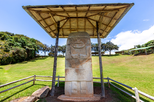 View of the ancient stone statue at San Agustin Archaeological Park protected by a wooden roof on a grassy hill in San Agustin Huila Colombia.