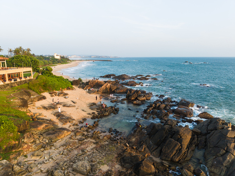 Aerial view of the rocky coastline and sandy beach with people walking near the turquoise ocean and lush green vegetation in Galle Southern Province Sri Lanka. Aerial view of the rocky coastline and sandy beach with people walking near the turquoise ocean and lush green vegetation in Galle Southern Province Sri Lanka.