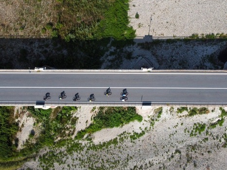 Aerial view of Ponte Crescentino with a group of cyclists riding across the bridge over a rocky riverbed in Verrua Savoia Piemonte Italy.