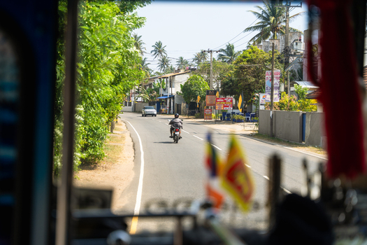 Sri Lanka 31 January 2026 View of a road through a vehicle window with a motorcyclist and lush tropical greenery.