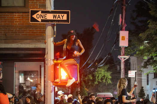 Brooklyn New York USA 14 June 2026 View of a woman sitting on a traffic light pole during Knicks championship celebrations in the street at night surrounded by a crowd of fans. Brooklyn New York USA 14 June 2026 View of a woman sitting on a traffic light pole during Knicks championship celebrations in the street at night surrounded by a crowd of fans.