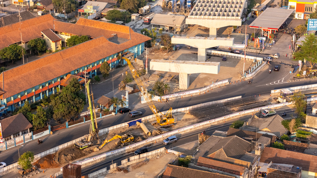 Indonesia 24 September 2026 Aerial view of a construction site for an elevated highway featuring heavy machinery cranes concrete pillars and surrounding urban infrastructure.
