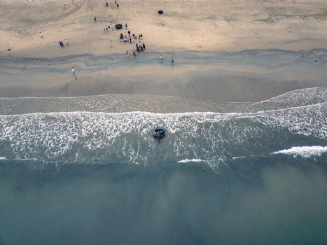 Aerial view of a traditional round basket boat in the surf with people gathered on the sandy beach in Vietnam. Aerial view of a traditional round basket boat in the surf with people gathered on the sandy beach in Vietnam.