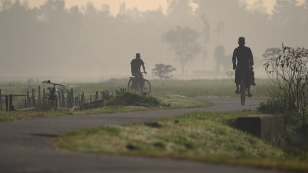 View of people cycling on a misty rural road in Bogura Bangladesh.