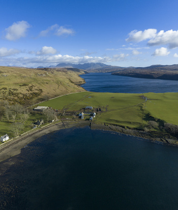 Aerial view of Gesto Bay Viewpoint with green pastures a small farm and the calm blue waters of the bay under a bright sky Isle of Skye Scotland United Kingdom.