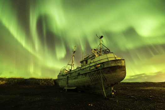 View of an old grounded wooden fishing boat under the vibrant green Northern Lights dancing across the starry night sky Olafsvik Snaefellsbaer Iceland.