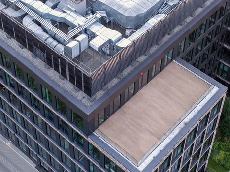 Aerial view of a modern office building rooftop featuring HVAC ventilation systems a wooden terrace deck and glass paneled exterior walls in Poland. Aerial view of a modern office building rooftop featuring HVAC ventilation systems a wooden terrace deck and glass paneled exterior walls in Poland.