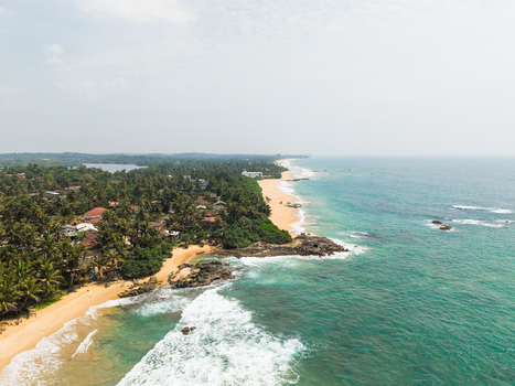 Aerial view of the tropical coastline featuring a sandy beach turquoise ocean waves and lush palm trees in Dodanduwa Southern Province Sri Lanka. Aerial view of the tropical coastline featuring a sandy beach turquoise ocean waves and lush palm trees in Dodanduwa Southern Province Sri Lanka.