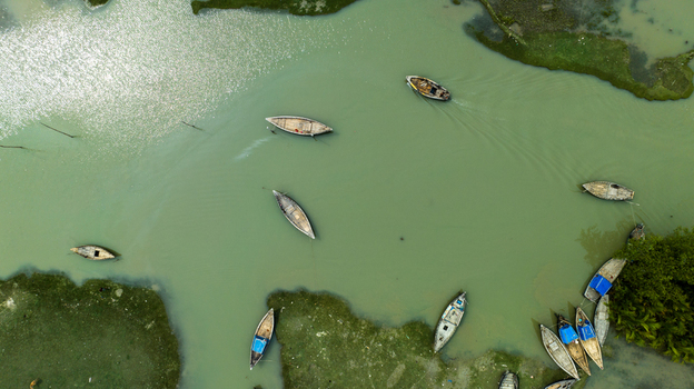 Aerial view of wooden boats navigating and moored along the green banks of the river in Patharghata Barisal Division Bangladesh. Aerial view of wooden boats navigating and moored along the green banks of the river in Patharghata Barisal Division Bangladesh.