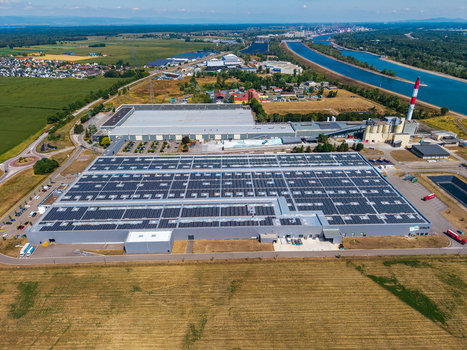 Aerial view of the Glas Trosch Alsace SAS industrial facility with solar panels on the roofs surrounded by agricultural fields and a canal in Hombourg Grand Est France.