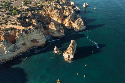 Aerial view of the dramatic limestone cliffs and sea stacks of Ponta da Piedade with turquoise water and kayakers exploring the coastline in Lagos Faro District Portugal.