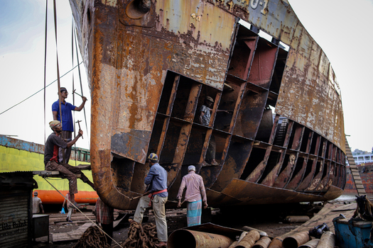 Keraniganj Bangladesh 31 August 2024 View of workers repairing a massive rusty ship hull at the Shipyard Dhaka with hammers and scaffolding in an industrial setting.