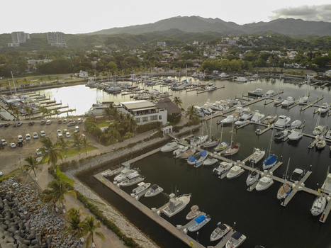 Aerial view of the marina with numerous boats docked at the piers surrounded by palm trees and buildings in La Cruz de Huanacaxtle Nayarit Mexico. Aerial view of the marina with numerous boats docked at the piers surrounded by palm trees and buildings in La Cruz de Huanacaxtle Nayarit Mexico.