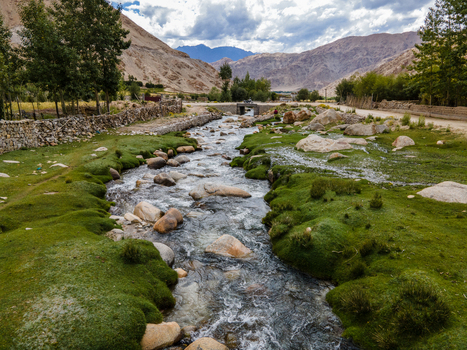 Aerial view of a stream flowing through the lush green landscape of Ladakh with rocky banks stone walls and distant mountains in Ladakh Division Ladakh India. Aerial view of a stream flowing through the lush green landscape of Ladakh with rocky banks stone walls and distant mountains in Ladakh Division Ladakh India.