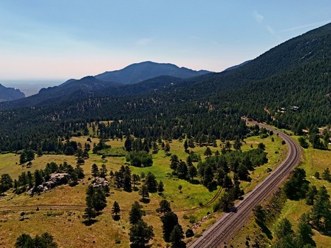 Aerial view of a scenic mountain landscape with dense pine forests rolling green meadows and railroad tracks winding through the valley in Golden Colorado United States. Aerial view of a scenic mountain landscape with dense pine forests rolling green meadows and railroad tracks winding through the valley in Golden Colorado United States.