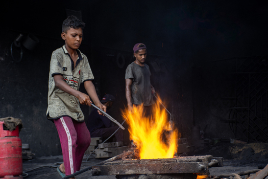 Bangladesh 28 August 2022 View of young workers melting metal over an open fire in a dark shipyard workshop.