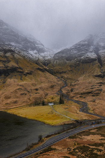 Aerial view of the iconic white house in Glencoe valley surrounded by snow capped mountains and a calm loch under a misty sky Glencoe Scotland United Kingdom. Aerial view of the iconic white house in Glencoe valley surrounded by snow capped mountains and a calm loch under a misty sky Glencoe Scotland United Kingdom.