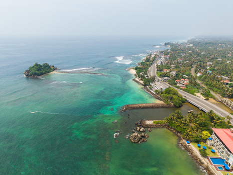 Aerial view of Devil s Rock island surrounded by turquoise ocean waters a coastal road and lush tropical greenery at Ahangama Southern Province Sri Lanka. Aerial view of Devil s Rock island surrounded by turquoise ocean waters a coastal road and lush tropical greenery at Ahangama Southern Province Sri Lanka.