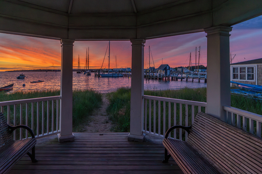 View of Martha s Vineyard harbor with sailboats moored at the docks under a vibrant sunset sky seen from a gazebo in Edgartown Massachusetts United States.