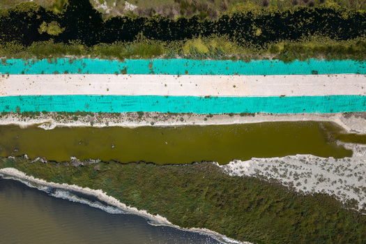 Aerial view of the Karavasta Lagoon featuring a white path with turquoise mesh alongside murky green water and natural wetlands in Divjake Fier County Albania.