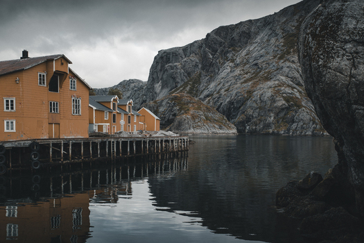 Nusfjord Nordland Norway 07 September 2022 View of historic Nusfjord fishing village with yellow wooden houses on stilts over calm water set against dramatic rocky cliffs. Nusfjord Nordland Norway 07 September 2022 View of historic Nusfjord fishing village with yellow wooden houses on stilts over calm water set against dramatic rocky cliffs.
