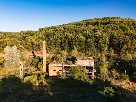 Aerial view of an abandoned coal loading facility and tall industrial tower amid forested hills in Rakoczibanya Hungary showing remnants of a mining settlement. Aerial view of an abandoned coal loading facility and tall industrial tower amid forested hills in Rakoczibanya Hungary showing remnants of a mining settlement.