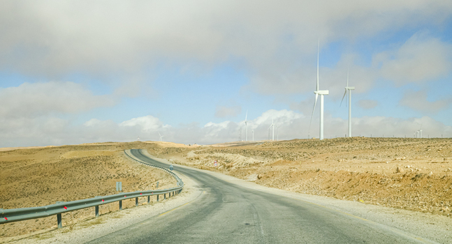 View of wind turbines along a winding road in the Wadi Rum Desert with arid terrain and a cloudy sky in Wadi Rum Village Aqaba Governorate Jordan. View of wind turbines along a winding road in the Wadi Rum Desert with arid terrain and a cloudy sky in Wadi Rum Village Aqaba Governorate Jordan.