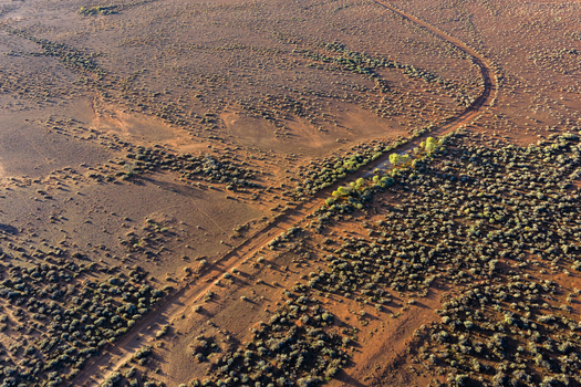 Aerial view of the vast outback landscape with red soil sparse green shrubs and a winding dirt track under warm sunlight Flinders Ranges South Australia Australia. Aerial view of the vast outback landscape with red soil sparse green shrubs and a winding dirt track under warm sunlight Flinders Ranges South Australia Australia.