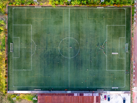 Aerial view of a soccer field with players on the green turf white markings and surrounding vegetation in Cilacap Central Java Indonesia. Aerial view of a soccer field with players on the green turf white markings and surrounding vegetation in Cilacap Central Java Indonesia.