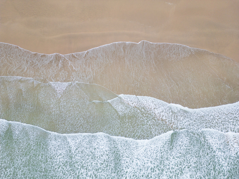 Aerial view of turquoise ocean waves with white foam breaking on the golden sandy beach in Polzeath Cornwall United Kingdom.