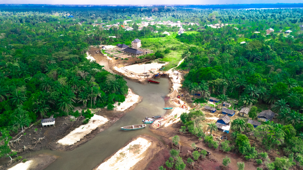Aerial view of Bukuma settlement in the Niger Delta featuring a winding river wooden boats on sandy banks lush vegetation and dwellings in Buguma Rivers Nigeria.